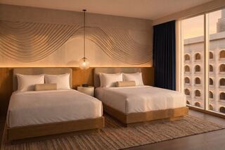 A serene hotel room features two beds, modern decor, and warm lighting, creating a relaxing atmosphere with natural wood tones.
