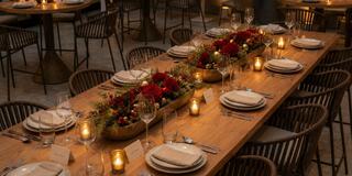 A beautifully set wooden table adorned with floral centerpieces, candles, and elegant dinnerware, creating a warm, inviting atmosphere.