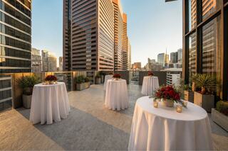A stylish rooftop venue with elegant tables adorned with floral arrangements, offering stunning views of a city skyline at sunset.