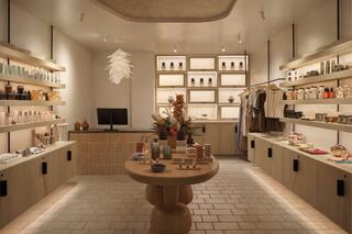 A modern, minimalist store features wooden shelves stocked with products, a round table centerpiece, and a cozy, inviting atmosphere.