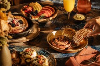 A beautiful brunch spread features fruit, pastries, and a refreshing drink, all arranged on a cozy table setting with warm lighting.