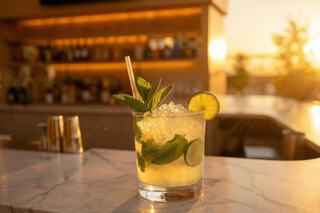 A refreshing cocktail with mint and lime sits on a marble bar, illuminated by warm sunset light.