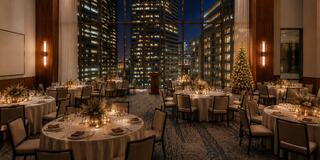 An elegant dining room filled with round tables, softly lit, featuring a Christmas tree and a stunning city skyline at night.
