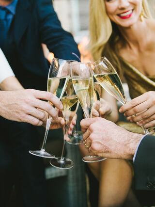 Glasses of champagne clink together in a festive toast, surrounded by elegantly dressed hands and cheerful smiles, capturing a joyful moment.