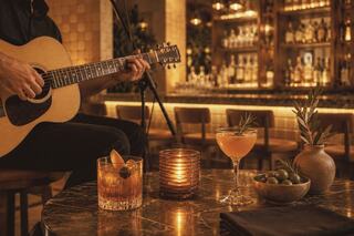 A cozy bar scene featuring a musician with an acoustic guitar, elegant cocktails, olives, and a warm candlelight ambiance.
