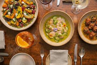 A vibrant spread of dishes includes colorful salads, a delicate seafood plate adorned with flowers, and a refreshing drink with an orange slice.
