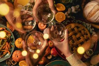 Glasses are clinking together amid a festive spread of pumpkins, delicious food, and warm lighting, celebrating togetherness and good times.