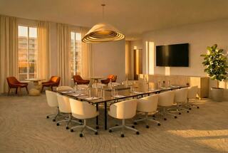A modern conference room features a long table, comfortable chairs, soft lighting, and a large screen, creating an inviting atmosphere.