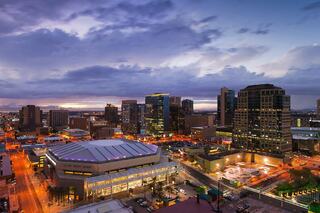 A vibrant city skyline lit up at dusk, featuring modern buildings and a lively street below, with a dramatic sky overhead.
