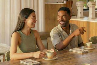 Two friends share laughs over coffee at a cozy, stylish café, enjoying a warm moment together. Sunlight adds to the cheerful ambiance.