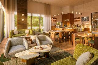 A cozy café interior with stylish furniture, warm lighting, and large windows offers a welcoming atmosphere for relaxation and socializing.