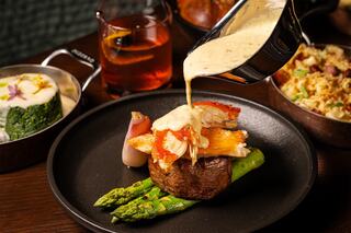 A succulent dish features a tender cut of meat topped with shrimp, asparagus, and a creamy sauce, accompanied by sides and a cocktail.
