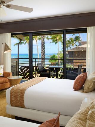 Bright and airy bedroom with two beds, tropical decor, and a view of palm trees and the ocean from a sliding glass door balcony.