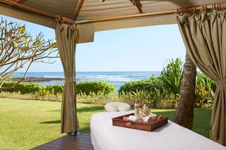 A serene outdoor massage setup overlooks the ocean, with a neatly arranged treatment table and fresh towels, surrounded by lush greenery.