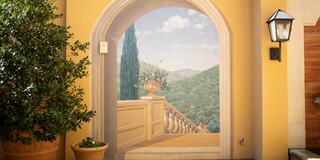 A painted archway reveals a scenic view of mountains, framed by a lush plant and a soft, warm wall tone, evoking tranquility.