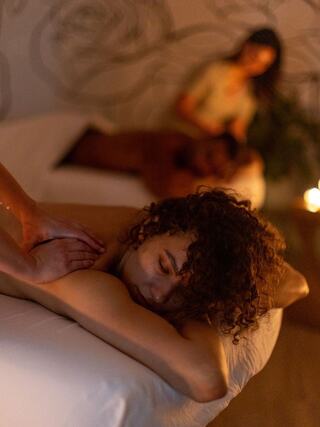 A serene spa scene with a person receiving a massage, while another therapist attends to a client in a soft, relaxing atmosphere.
