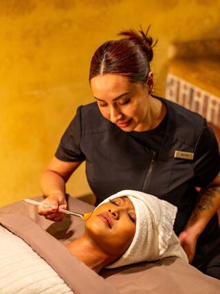 A skincare professional applies treatment to a client's face, creating a calming atmosphere in a spa setting.