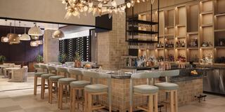 A stylish bar features light wood stools, elegant lighting, and a vast array of drinks on display, creating a sophisticated atmosphere.