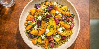 A vibrant salad featuring roasted colorful vegetables, toasted seeds, and crumbled cheese, garnished with herbs, in a rustic bowl.
