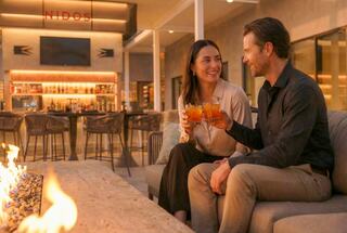 A couple enjoys drinks together in a cozy, modern lounge, smiling at each other amidst a warm, inviting atmosphere.