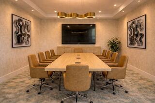 A modern conference room with a long wooden table, beige chairs, a large TV, and abstract artwork on the walls, creating a professional atmosphere.