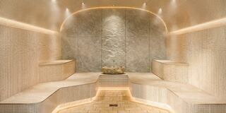 A serene, spacious steam room featuring textured stone walls, soft ambient lighting, and carved seating, creating a tranquil relaxation space.