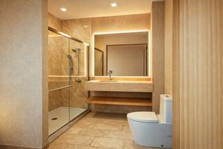 A modern bathroom featuring a glass shower, sleek vanity with backlit mirror, and a contemporary toilet, all in warm, neutral tones.