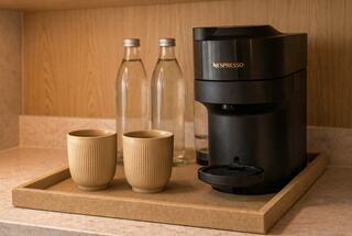 A sleek Nespresso machine sits on a tray beside two beige cups and two glass bottles, showcasing a minimalist coffee setup.