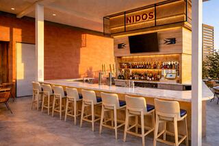 A stylish bar area features a marble counter, high stools, and a well-stocked shelf of drinks, illuminated by warm sunset lighting.