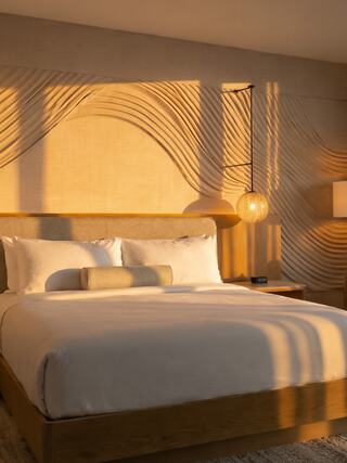 A cozy bedroom features a stylish wooden bed, textured wall design, and warm, ambient lighting, creating a serene and inviting atmosphere.