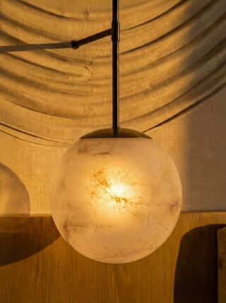A round, translucent pendant light emits a warm glow, set against a backdrop of soft draped fabric and a wooden surface.