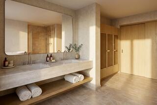 A modern bathroom with dual sinks, wooden accents, rolled towels, natural light, and a spacious shower area, creating a serene atmosphere.