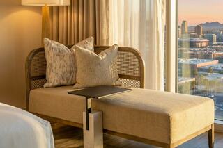 A stylish chaise lounge with plush cushions and a modern side table overlooks a scenic view, bathed in warm light from large windows.