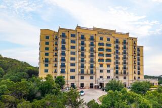A large, yellow multi-story hotel building surrounded by lush greenery and trees against a bright sky.