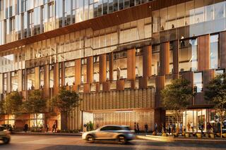 A modern building features large glass windows, wooden accents, and landscaping, with people walking and cars passing by.