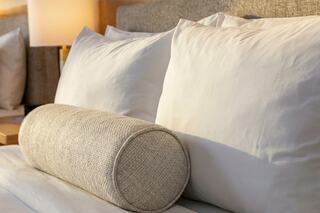 A neatly arranged bed features fluffy white pillows and a textured cylindrical bolster, creating a cozy and inviting atmosphere.