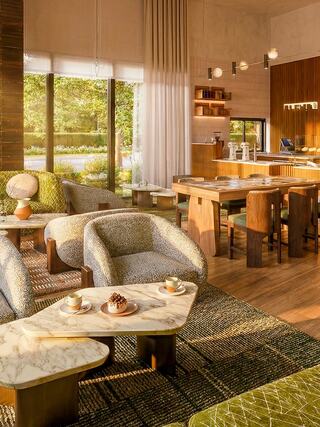 A stylish, modern lounge with cozy chairs, marble tables, and a warm, inviting ambiance, featuring large windows overlooking a garden.