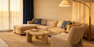 A cozy living room features a beige sectional sofa, patterned pillows, a round coffee table, and a stylish floor lamp, with soft lighting.