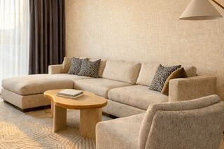 A cozy living area featuring a light-toned sectional sofa with decorative pillows, a round wooden coffee table, and soft textures throughout.