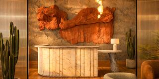 A modern reception area features a textured red wall, sleek marble furniture, stylish lighting, and potted cacti for a warm, inviting ambiance.