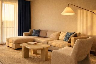 A cozy living space features a beige sectional sofa with decorative pillows, a wooden coffee table, and a warm, inviting atmosphere.