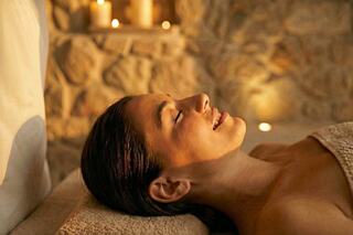 A woman relaxes on a massage table, illuminated by soft candlelight, with a serene expression and glowing skin.