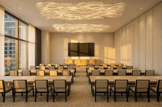 A modern conference room featuring rows of tables and chairs, large windows, and elegant lighting fixtures, creating a bright, professional space.