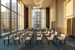 A spacious meeting room with rows of cream-colored chairs, large windows, and modern décor, illuminated by soft morning light.