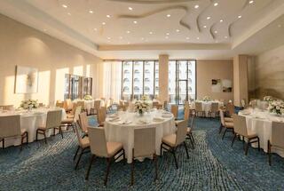 A sophisticated banquet hall features elegantly set round tables, floral centerpieces, and large windows allowing natural light to fill the space.