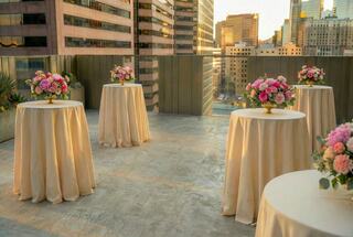 Elegant tables adorned with floral arrangements overlook a city skyline during sunset, creating a beautiful and sophisticated atmosphere.