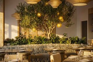 A stylish dining area features a cozy sofa, tables, lush greenery, and hanging lights, creating a warm and inviting atmosphere.
