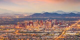A vibrant cityscape at dusk, with gleaming skyscrapers and a backdrop of mountains, painted in soft hues of orange and purple.