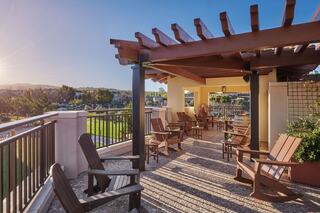 A serene balcony with wooden chairs and a pergola, surrounded by greenery and bathed in warm sunlight, perfect for relaxation.