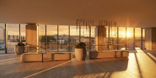 A sunlit lobby features modern decor, large windows framing a sunset, and elegant planters, creating a warm, inviting atmosphere.